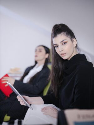 Two professional women in a modern office setting engaged with technology and reading materials.
